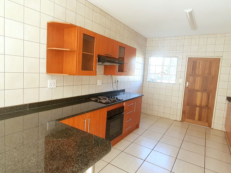 A functional kitchen featuring wooden cabinetry, granite countertops, a built-in oven, hob, and extractor fan, with tiled walls and flooring throughout.