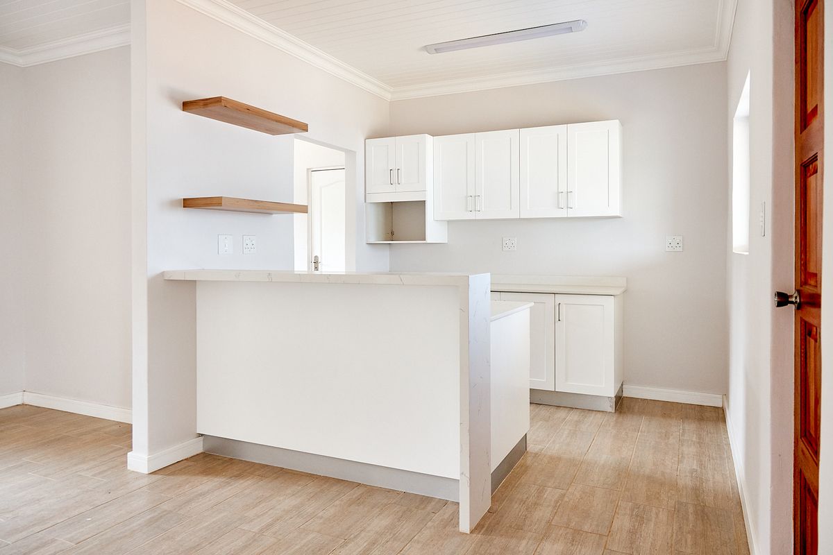 A bright, modern kitchen featuring white cabinetry, stone-look countertops, a breakfast bar, and wood-look tile flooring in a clean, minimalist space.