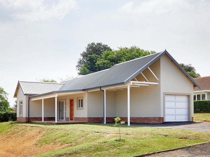 A modern townhouse exterior featuring a metal roof, brick base, covered patio area, and an integrated garage with a paved driveway.