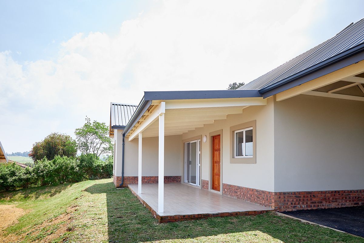 A well-maintained rear exterior view of the townhouse featuring a covered patio with tiled flooring, brick detailing, and a sliding glass door entrance.