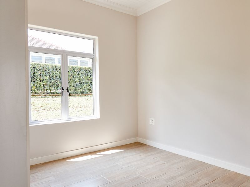 A bright, empty bedroom featuring neutral walls, tiled flooring, and a large window overlooking the garden area.