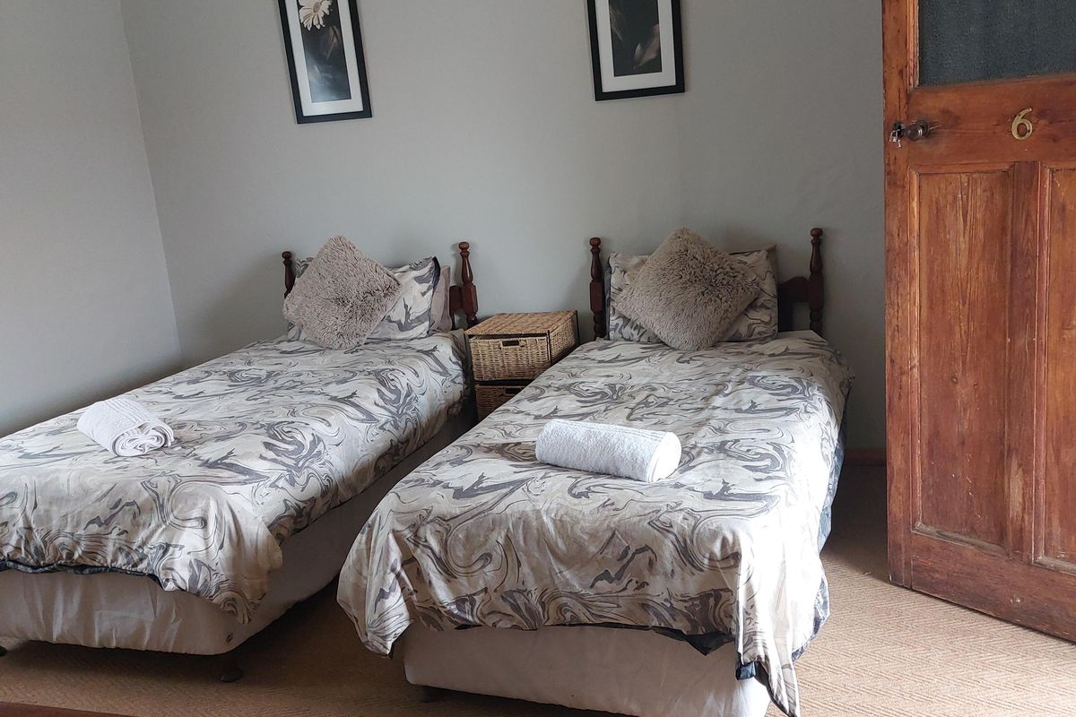 A hotel bedroom featuring twin beds, neutral wall tones, and a traditional wooden door with a brass number plate.