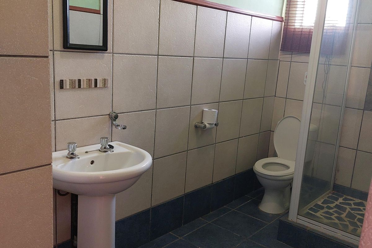 A functional bathroom featuring a pedestal basin, a glass-enclosed shower, and a toilet, finished with tiled walls and flooring.