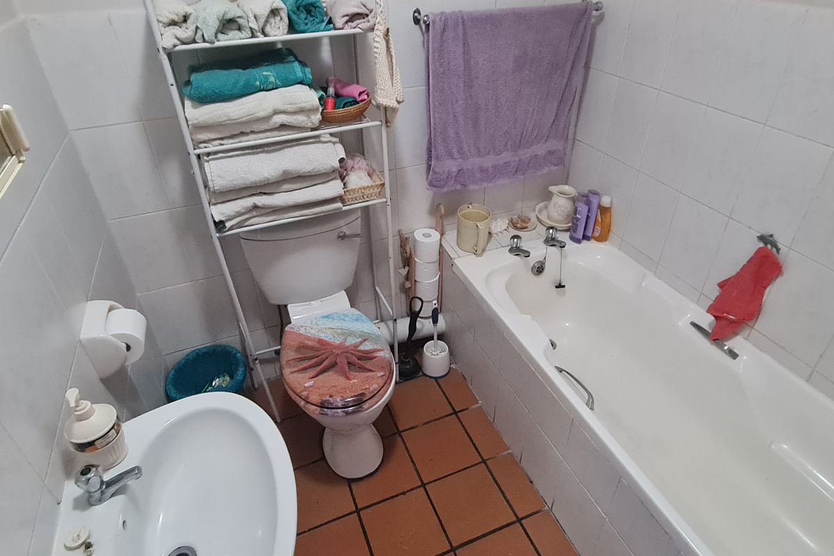 A compact bathroom featuring a standard bathtub, pedestal basin, and toilet with white wall tiling and terracotta floor tiles.
