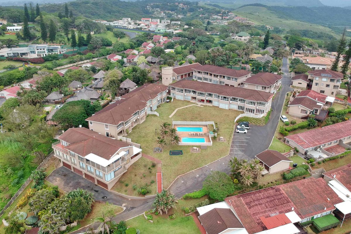 Aerial view of a residential apartment complex featuring a central swimming pool, landscaped garden areas, and paved parking facilities within a suburban estate.