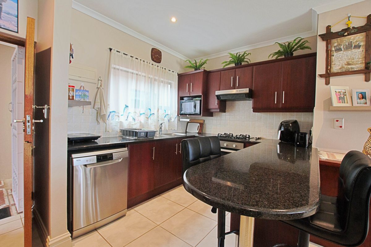 A functional kitchen featuring dark wood cabinetry, granite countertops, a breakfast bar, and integrated appliances including a gas hob and extractor fan.