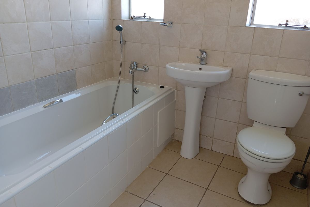 A functional bathroom featuring a standard bathtub with handheld shower attachment, a pedestal basin, and a toilet, finished with neutral wall and floor tiling.