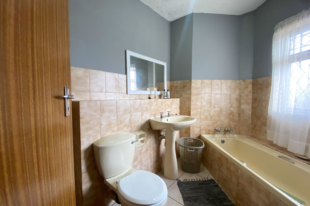 A functional bathroom featuring a classic bathtub, pedestal basin, and toilet with neutral wall tiling and grey painted upper walls.