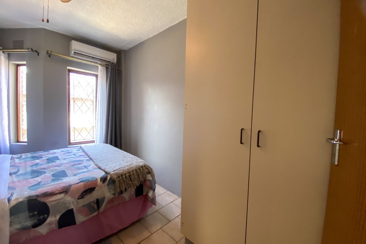 A bedroom featuring built-in cupboards, tiled flooring, a ceiling fan, and a wall-mounted air conditioning unit.