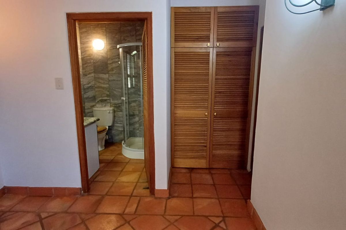 Bedroom featuring terracotta floor tiles, built-in wooden louvered closets, and direct access to an en-suite bathroom with a shower.