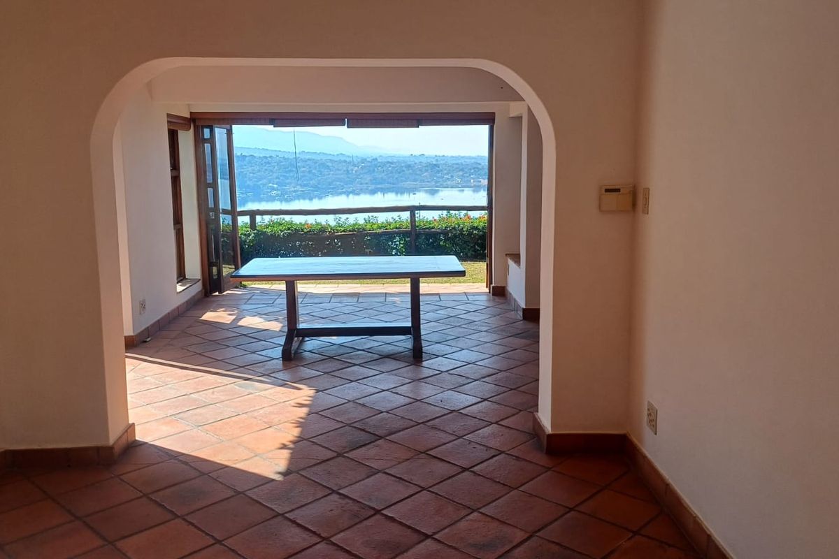 Spacious living area featuring terracotta floor tiles and an arched transition to an open balcony with scenic water views.