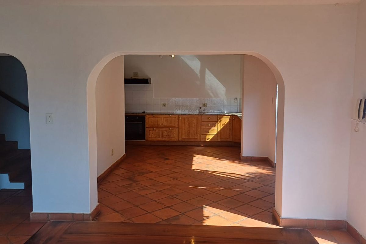 A view through an archway into a kitchen featuring wooden cabinetry, tiled flooring, and built-in appliances.