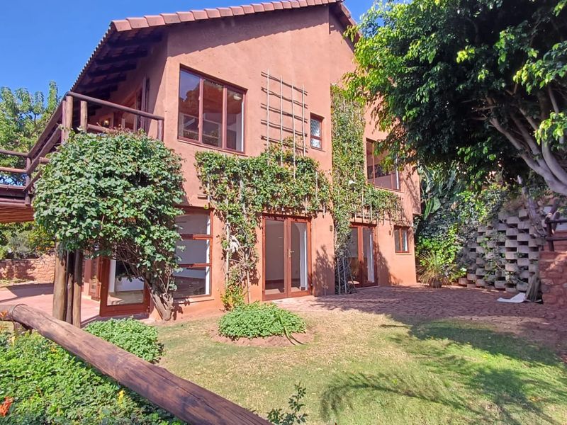 Rear view of a multi-level house featuring a timber balcony, paved patio area, and established garden surroundings.