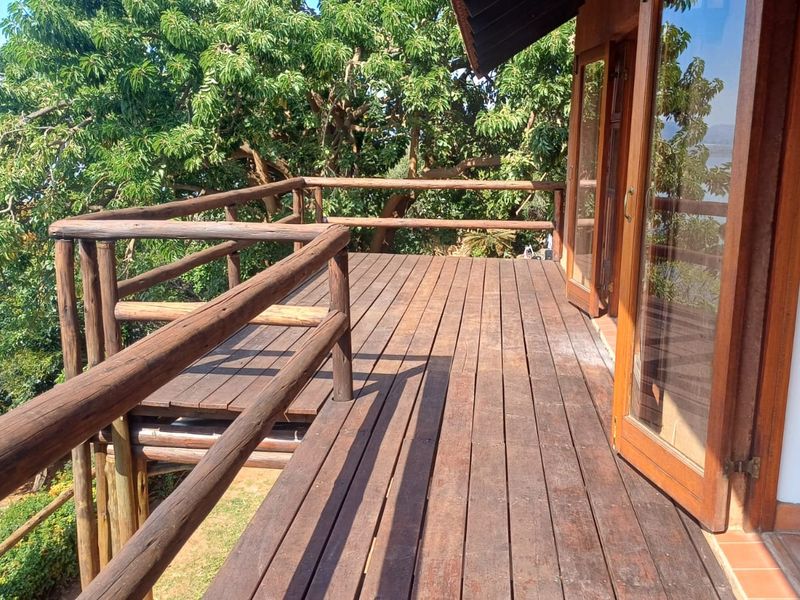 A spacious wooden balcony featuring a timber balustrade and large glass sliding doors, offering an elevated outdoor space with lush garden views.