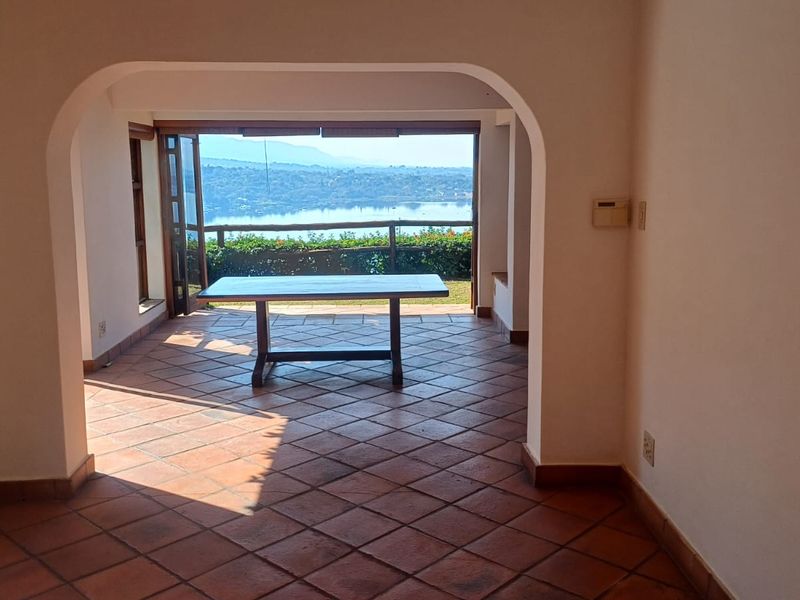 Spacious living area featuring terracotta floor tiles and an arched transition to an open balcony with scenic water views.