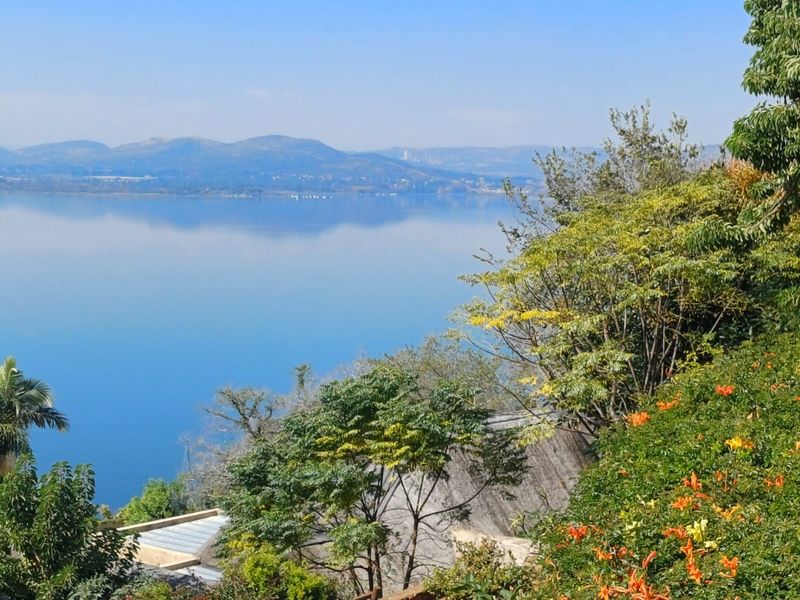 Scenic elevated view overlooking a large tranquil lake with distant mountain ranges and lush surrounding vegetation.