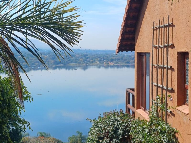 A scenic view of a calm lake framed by the terracotta exterior of the house, featuring wooden architectural details and lush surrounding greenery.