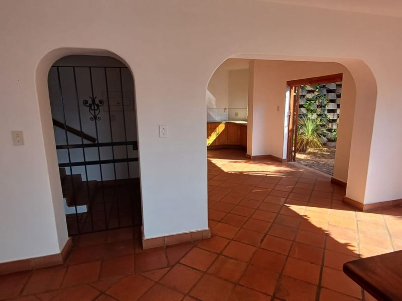 Open plan living area featuring terracotta floor tiles and arched doorways leading to a kitchen and outdoor patio space.