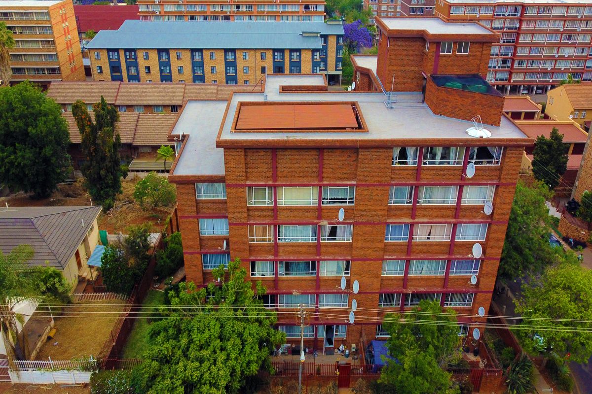 Aerial view of a multi-story brick apartment building featuring a flat roof, multiple satellite dish installations, and surrounding residential grounds.