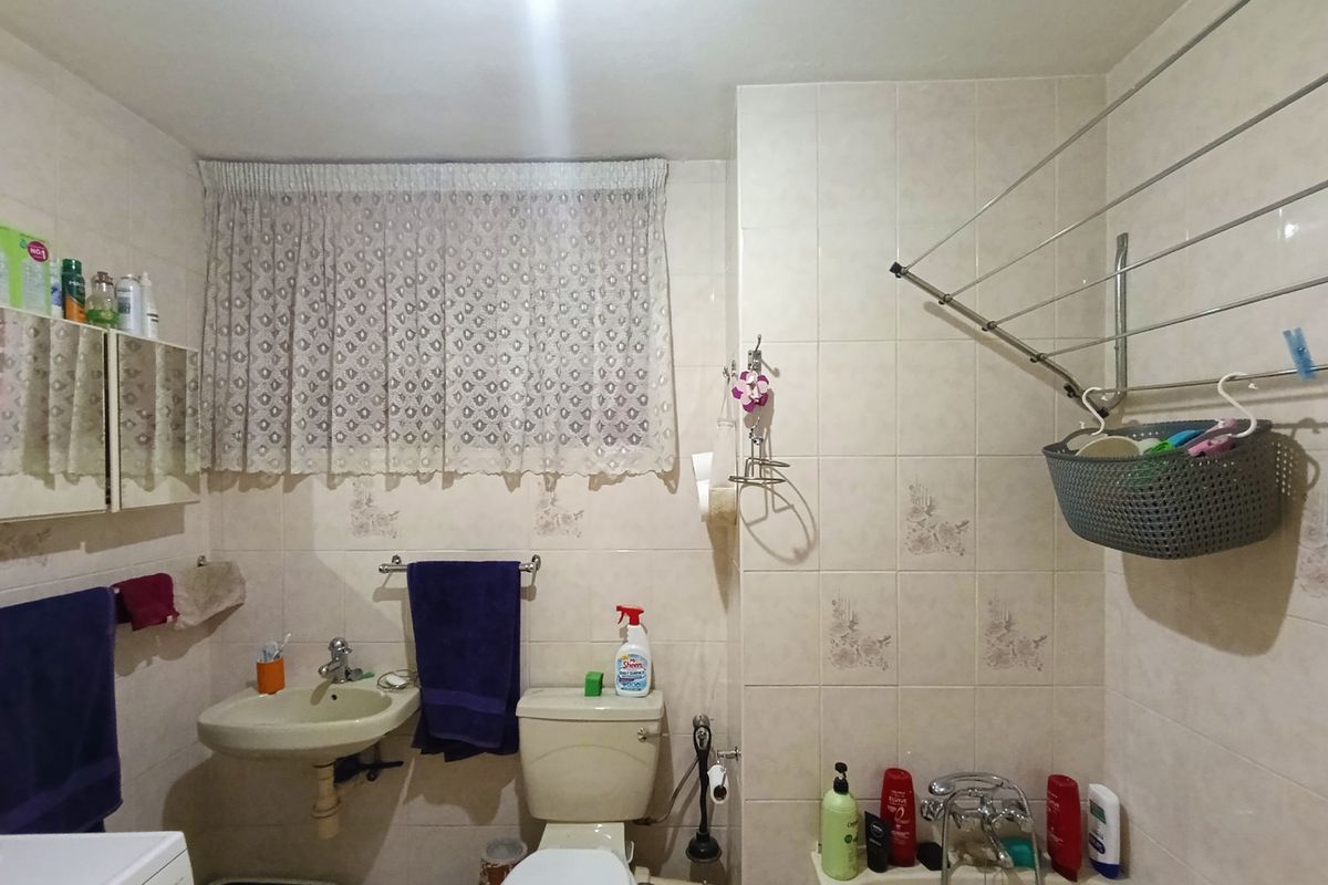 A functional bathroom featuring a pedestal basin, toilet, and wall-mounted drying rack, finished with dated wall tiling throughout.