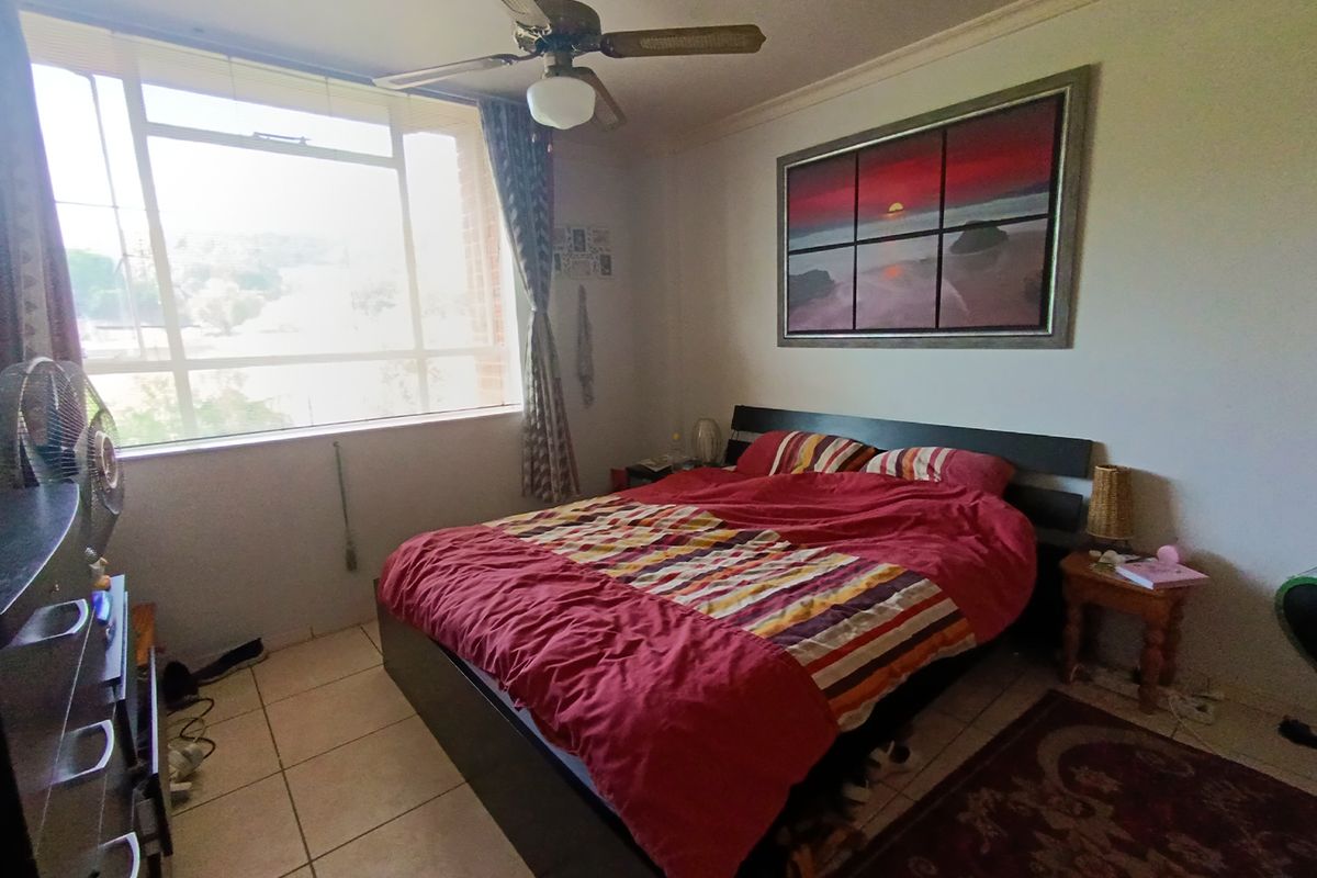 A functional bedroom featuring tiled flooring, a ceiling fan, and a large window providing natural light.