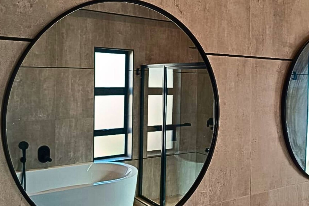 Modern bathroom featuring a freestanding bathtub, glass shower enclosure, and dual round mirrors with contemporary black fixtures and neutral wall tiling.