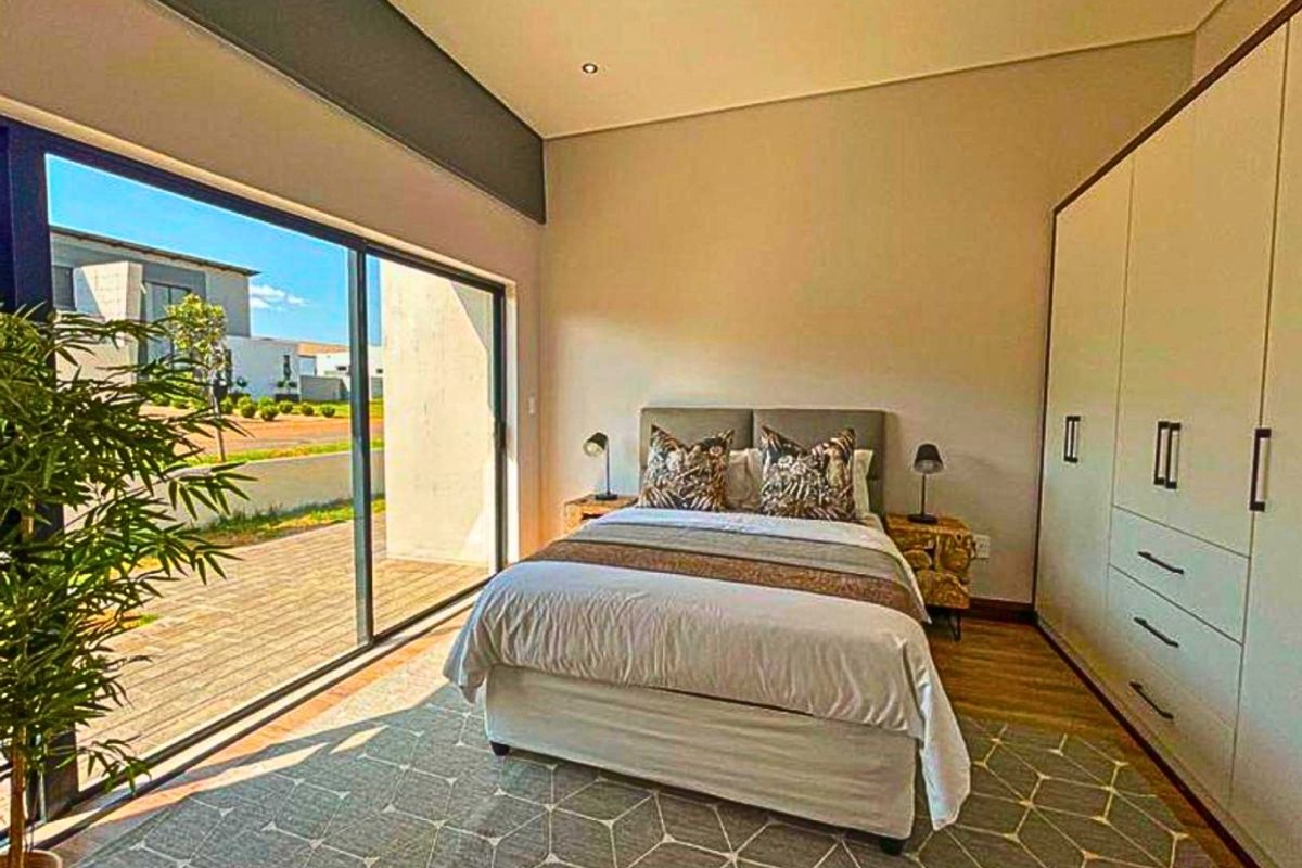 Modern bedroom featuring built-in wardrobes, laminate flooring, and large sliding glass doors providing direct access to the outdoor patio area.