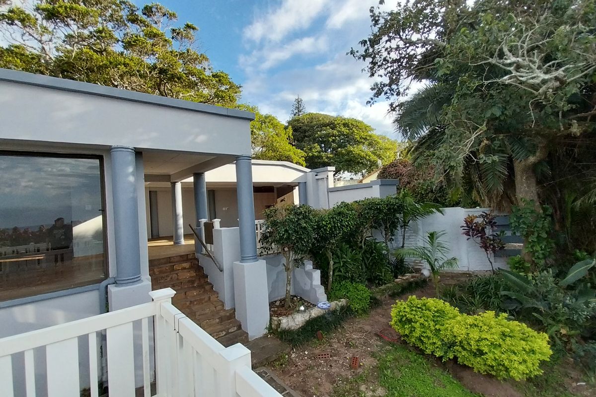 A view of the rear exterior of the house featuring a covered patio area with columns, stone steps, and an adjacent garden space.