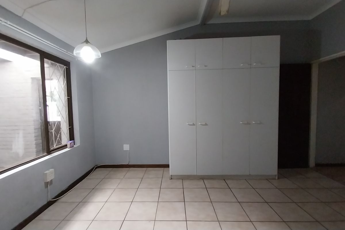 A bedroom featuring built-in wardrobes, tiled flooring, and a large window with security bars, providing a functional and neutral living space.
