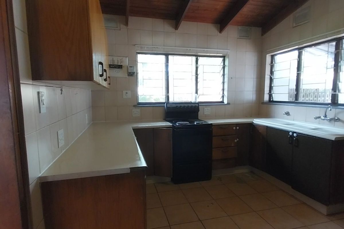 A dated kitchen featuring wooden cabinetry, tiled splashbacks, a freestanding stove, and exposed timber ceiling beams.