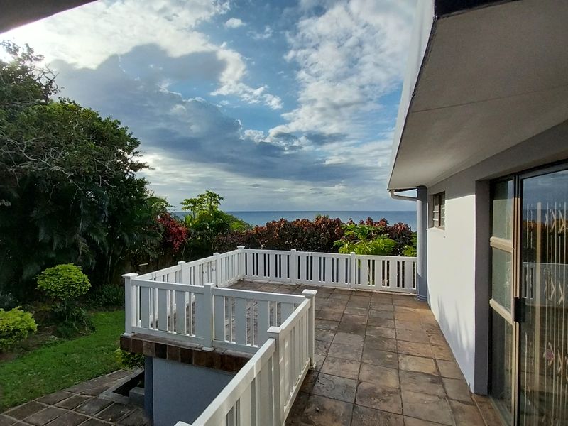 A spacious outdoor patio area featuring tiled flooring, white balustrades, and elevated views of the surrounding garden and ocean horizon.