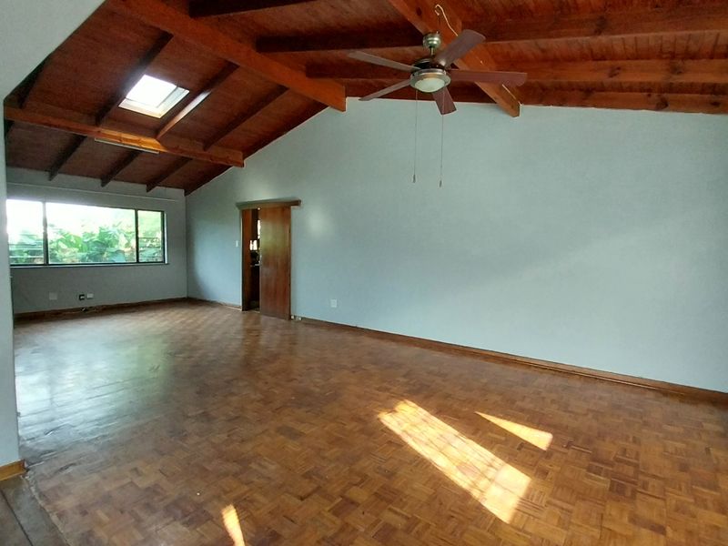 Spacious living area featuring high vaulted timber ceilings, exposed wooden beams, a skylight, ceiling fan, and classic parquet flooring.