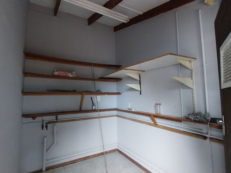 A functional utility or laundry space featuring wall-mounted shelving, exposed plumbing connections, and tiled flooring.