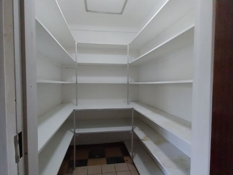 A walk-in pantry or scullery area featuring extensive built-in white shelving and tiled flooring, providing ample storage space for kitchen essentials.