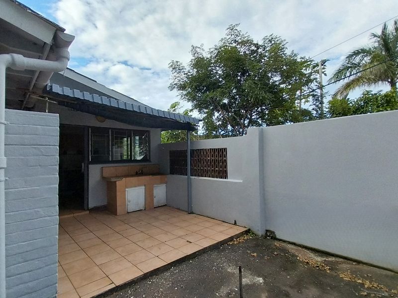 A covered outdoor patio area featuring a built-in brick workstation with a sink, adjacent to a private boundary wall.