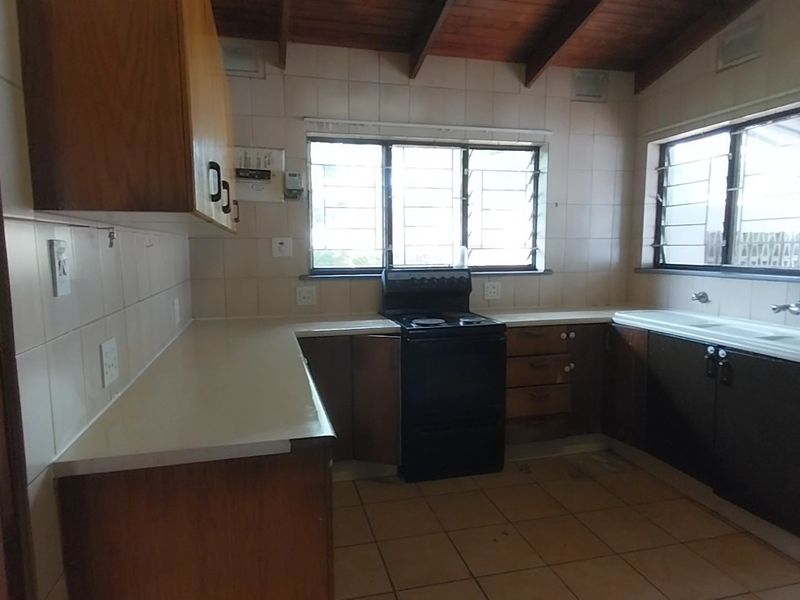 A dated kitchen featuring wooden cabinetry, tiled splashbacks, a freestanding stove, and exposed timber ceiling beams.