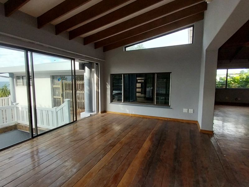 Spacious living area featuring exposed timber ceiling beams, large sliding glass doors, and polished hardwood flooring with views of the exterior.