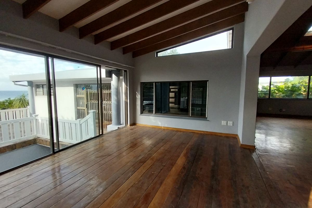 Spacious living area featuring exposed timber ceiling beams, large sliding glass doors, and polished hardwood flooring with views of the exterior.