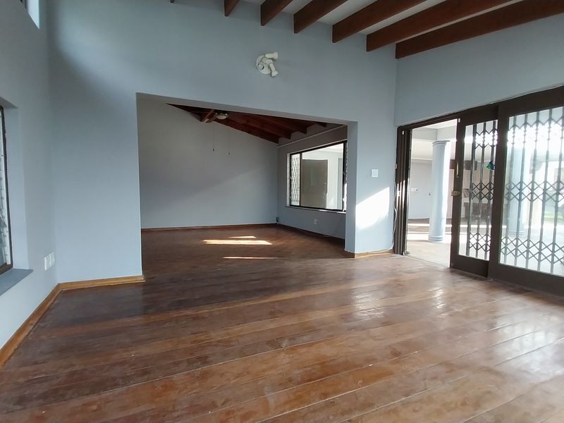 Spacious open-plan living area featuring exposed timber ceiling beams, polished wooden flooring, and large sliding doors leading to an outdoor patio.