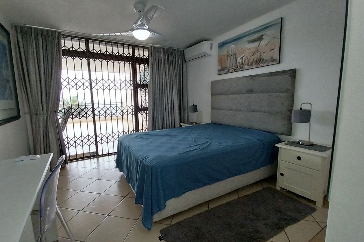 A well-maintained bedroom featuring tiled flooring, a ceiling fan, a wall-mounted air conditioner, and a secure sliding gate leading to an outdoor area.