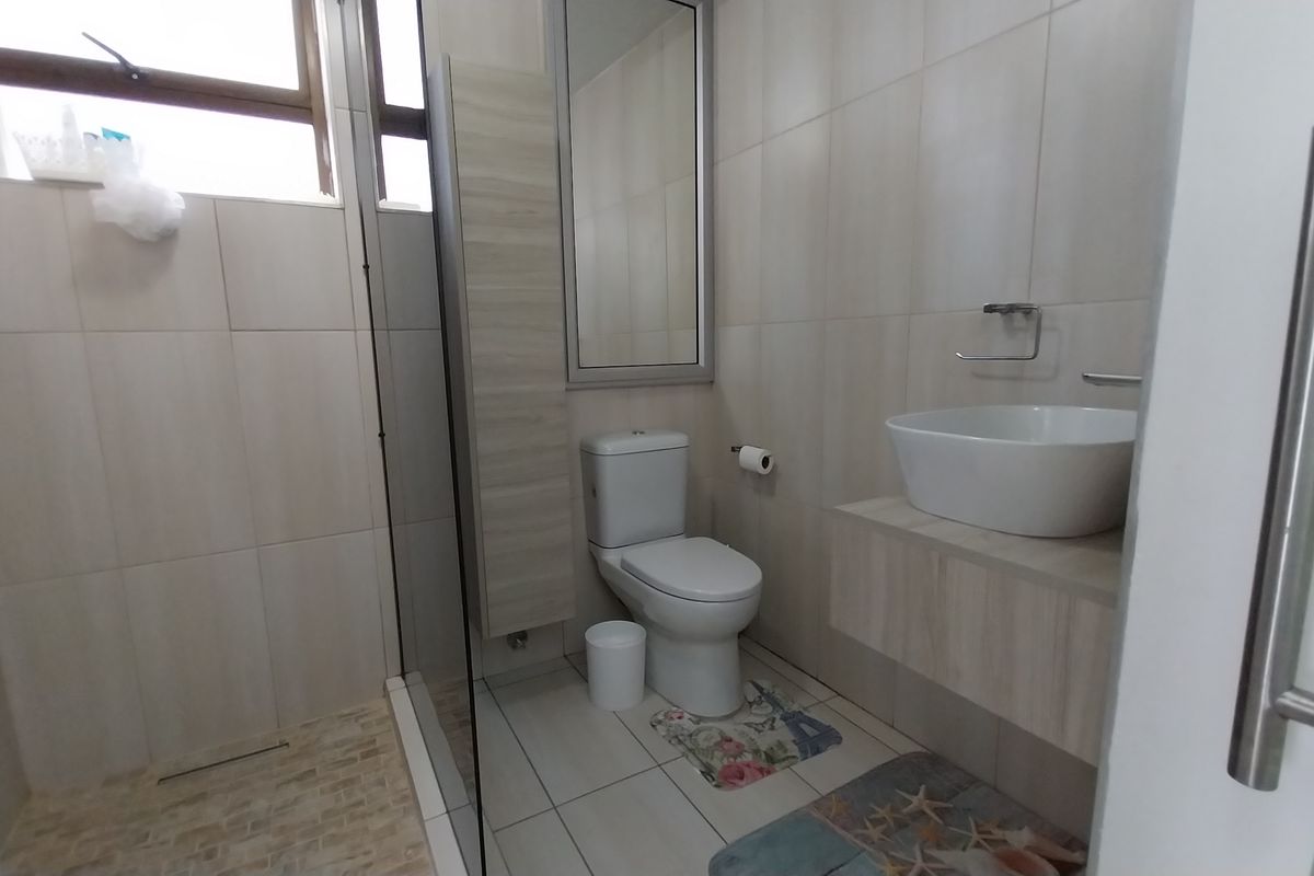 Modern bathroom featuring a walk-in shower with glass screen, wall-mounted vanity with vessel sink, and neutral floor-to-ceiling tiling.