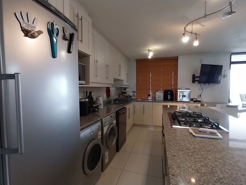 Open-plan kitchen featuring granite countertops, built-in cabinetry, gas hob, and tiled flooring, seamlessly flowing into the living area with access to the balcony.