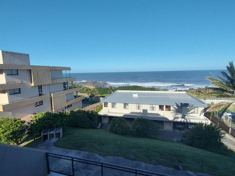 An elevated view overlooking the coastal landscape, neighbouring apartment buildings, and the ocean horizon.
