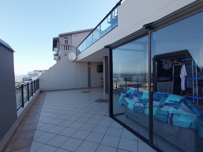 A spacious balcony featuring tiled flooring, a modern glass balustrade, and large sliding glass doors providing seamless indoor-outdoor flow.
