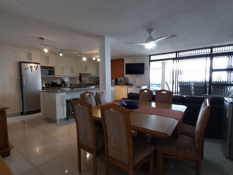 Spacious open-plan living, dining, and kitchen area featuring tiled floors, modern cabinetry, and direct access to an outdoor balcony through sliding glass doors.
