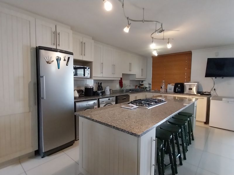 Spacious kitchen featuring white cabinetry, granite countertops, a central island with a gas hob, and tiled flooring throughout.