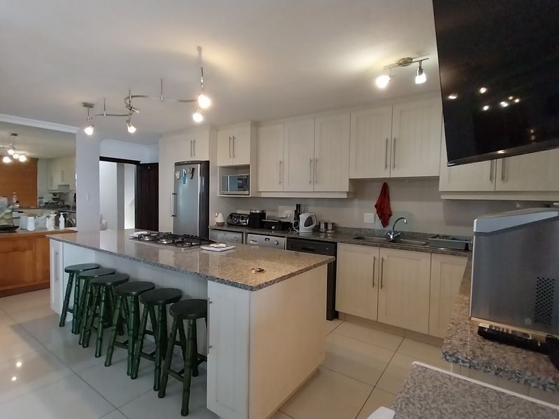 Spacious kitchen featuring a large central island with a gas hob, granite countertops, ample cabinetry, and tiled flooring throughout.