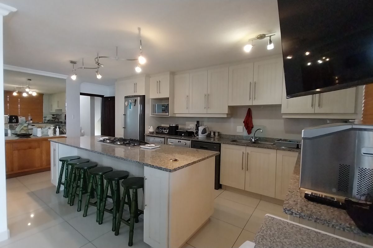 Spacious kitchen featuring a large central island with a gas hob, granite countertops, ample cabinetry, and tiled flooring throughout.