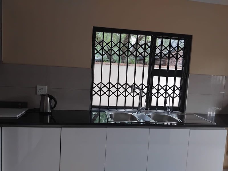 A clean kitchen area featuring modern white cabinetry, a dark granite countertop, and a double sink with a security gate installed on the window.
