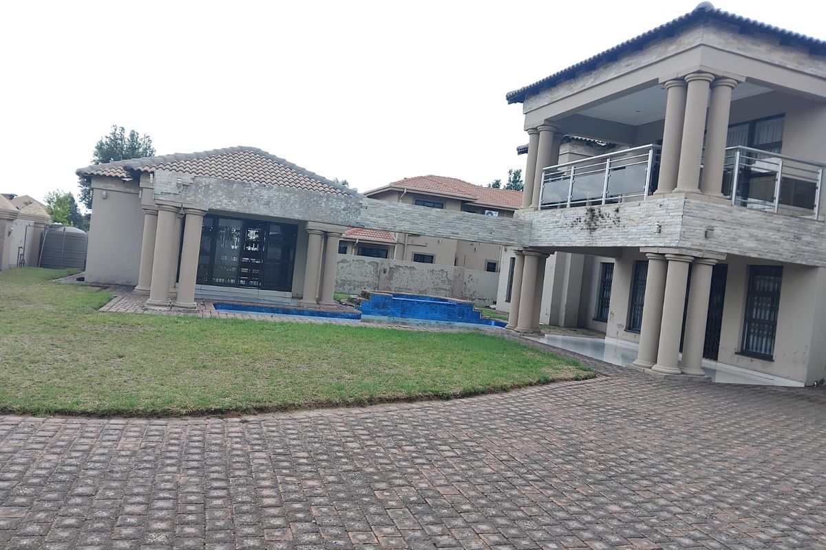 Rear exterior view of a multi-story house featuring a swimming pool, stone-clad columns, and a paved courtyard area.